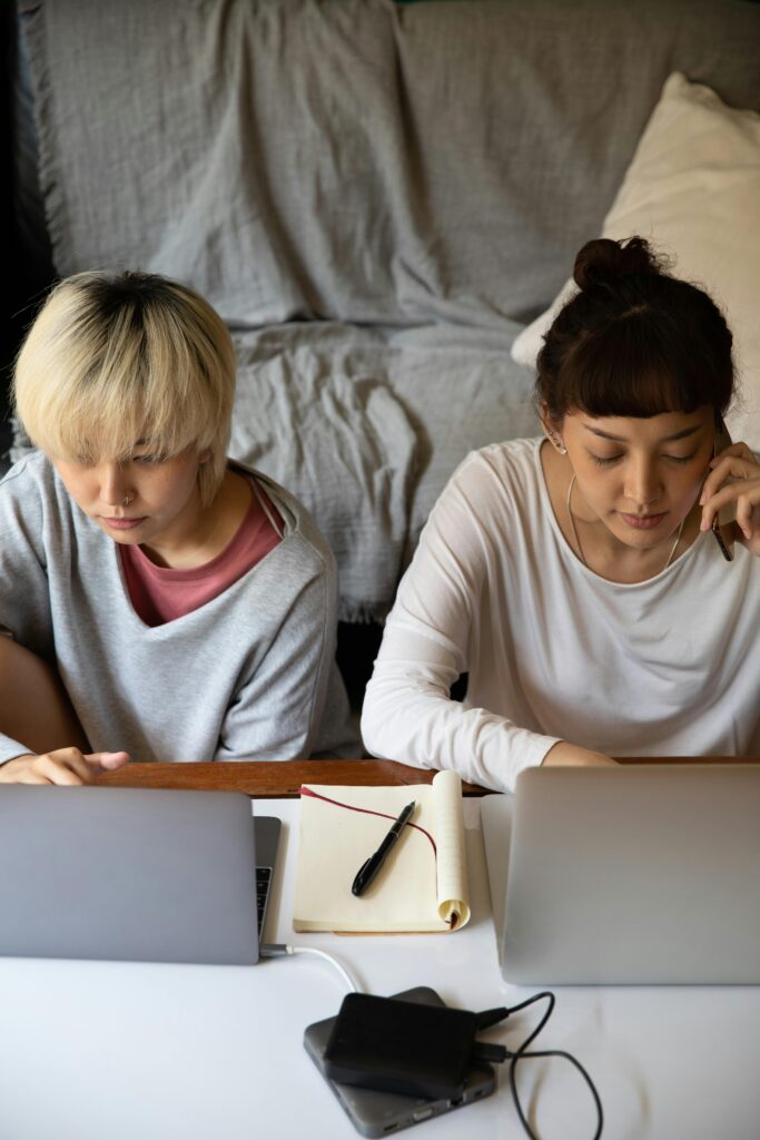Globally_ Services_1 Top view of young multiracial female students in casual wear browsing internet on netbooks while sitting near copybook and hard drive in apartment