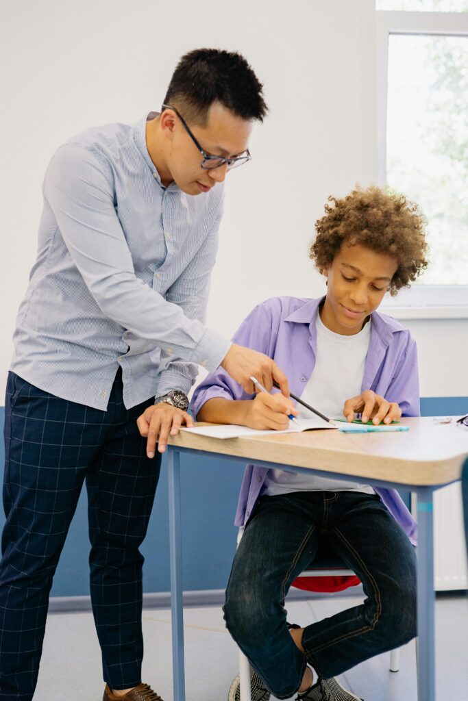 Globally_ Services_3 Teacher guiding student with coursework in a classroom environment.